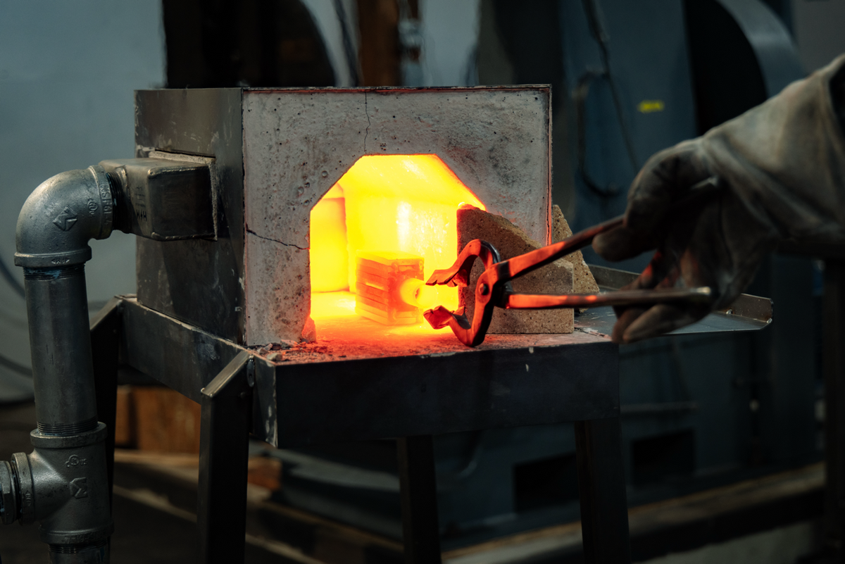 Tongs holding a glowing, red-hot blade at the mouth of a forge
