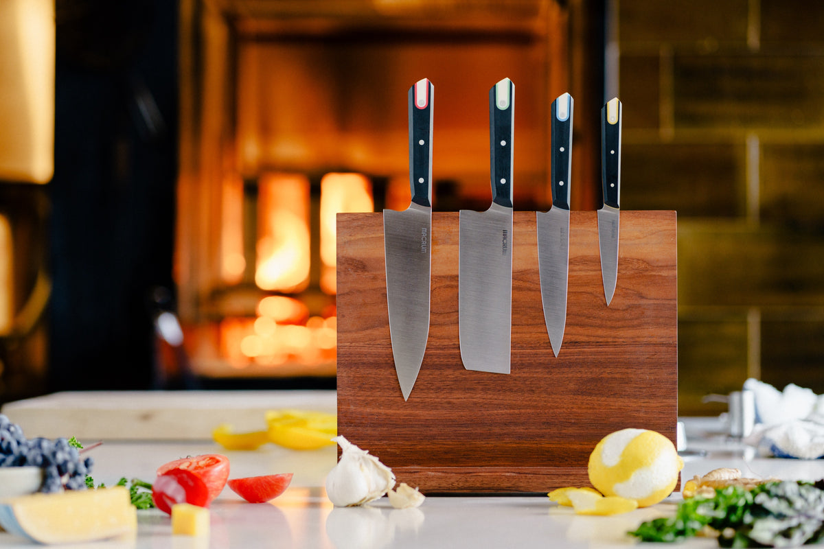 The four Macrum kitchen knives, with red, green, blue and yellow handle liners, on a walnut knife stand